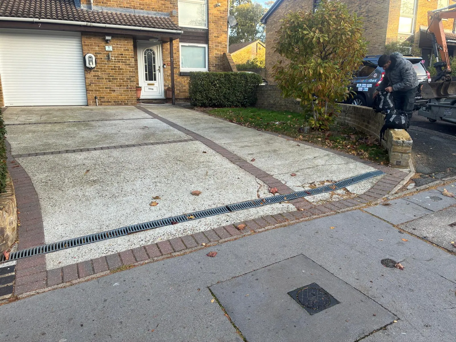 Original weathered concrete driveway with reddish dividing strips and cracks near the entrance